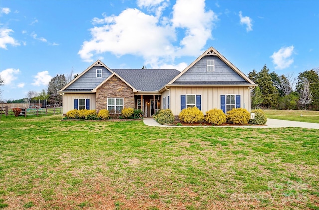 view of front of property featuring stone siding, board and batten siding, a front yard, and fence