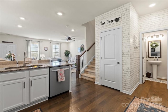 kitchen featuring dark wood-type flooring, a sink, brick wall, dark stone countertops, and dishwasher