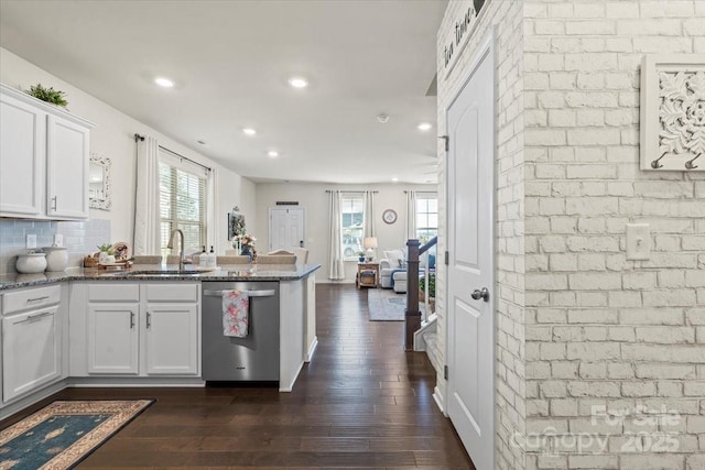 kitchen with a peninsula, a sink, white cabinetry, stainless steel dishwasher, and dark wood finished floors