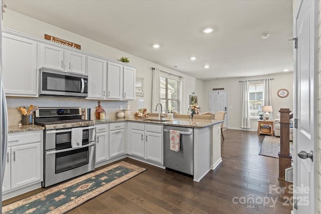 kitchen with a peninsula, tasteful backsplash, appliances with stainless steel finishes, and dark wood-style flooring