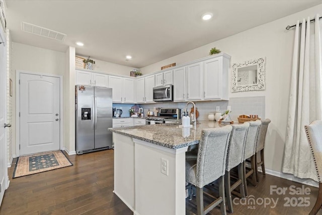 kitchen featuring visible vents, white cabinets, a peninsula, light stone countertops, and stainless steel appliances