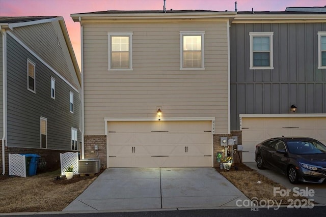 back of property at dusk with board and batten siding, central AC, driveway, and an attached garage