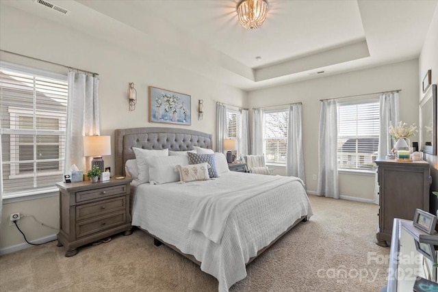 bedroom featuring a tray ceiling, visible vents, light carpet, and baseboards