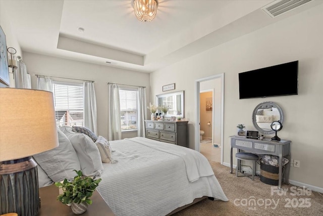 bedroom with ensuite bathroom, light carpet, visible vents, baseboards, and a tray ceiling