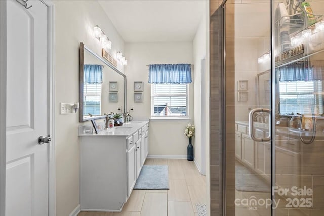 full bath featuring double vanity, tiled shower, a sink, and baseboards