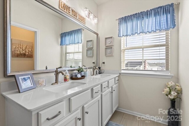 full bath with double vanity, baseboards, and a sink