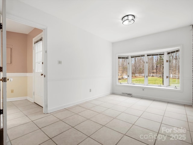 empty room featuring light tile patterned floors, visible vents, and baseboards