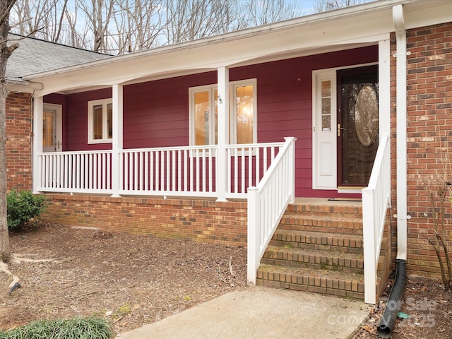 entrance to property featuring a porch, brick siding, and a shingled roof