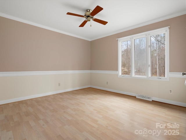 empty room with visible vents, crown molding, light wood-type flooring, and baseboards