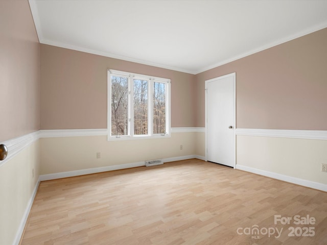 empty room with light wood-style flooring, visible vents, baseboards, and ornamental molding