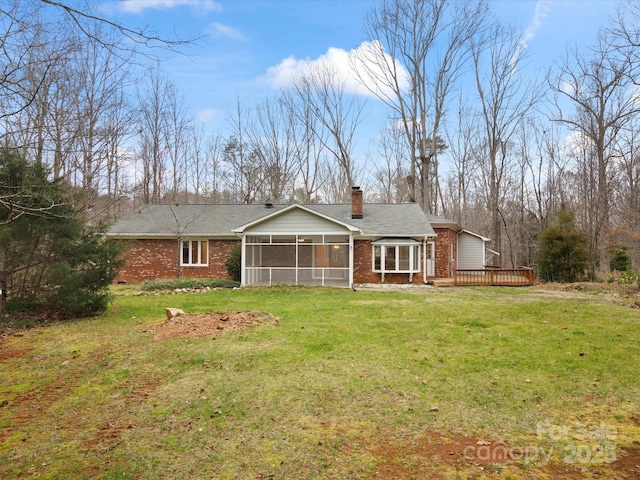 rear view of house featuring brick siding, a lawn, a chimney, a deck, and a sunroom