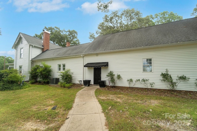 back of house with a yard, central AC, and roof with shingles