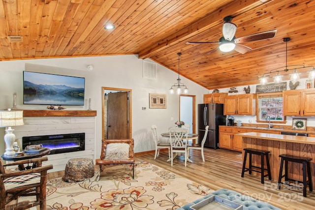 living area featuring vaulted ceiling with beams, wooden ceiling, a ceiling fan, light wood-style floors, and a glass covered fireplace