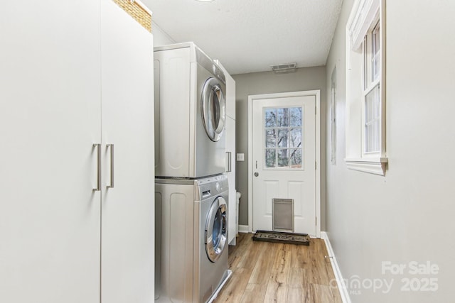 laundry area with laundry area, baseboards, visible vents, stacked washer / dryer, and light wood-style floors