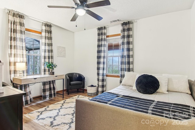 bedroom with a textured ceiling, ceiling fan, wood finished floors, visible vents, and baseboards