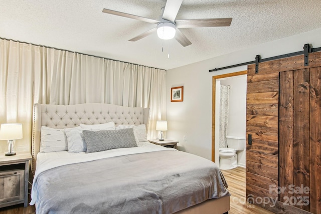 bedroom featuring a barn door, a ceiling fan, ensuite bath, wood finished floors, and a textured ceiling