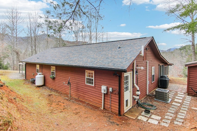 view of property exterior with a shingled roof and central AC