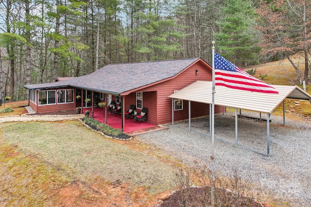 exterior space with a shingled roof, gravel driveway, a wooded view, and a sunroom