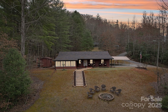 view of front of house featuring an outdoor fire pit, a view of trees, and an outdoor structure