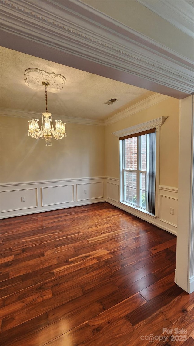 spare room with dark wood finished floors, a notable chandelier, visible vents, ornamental molding, and wainscoting