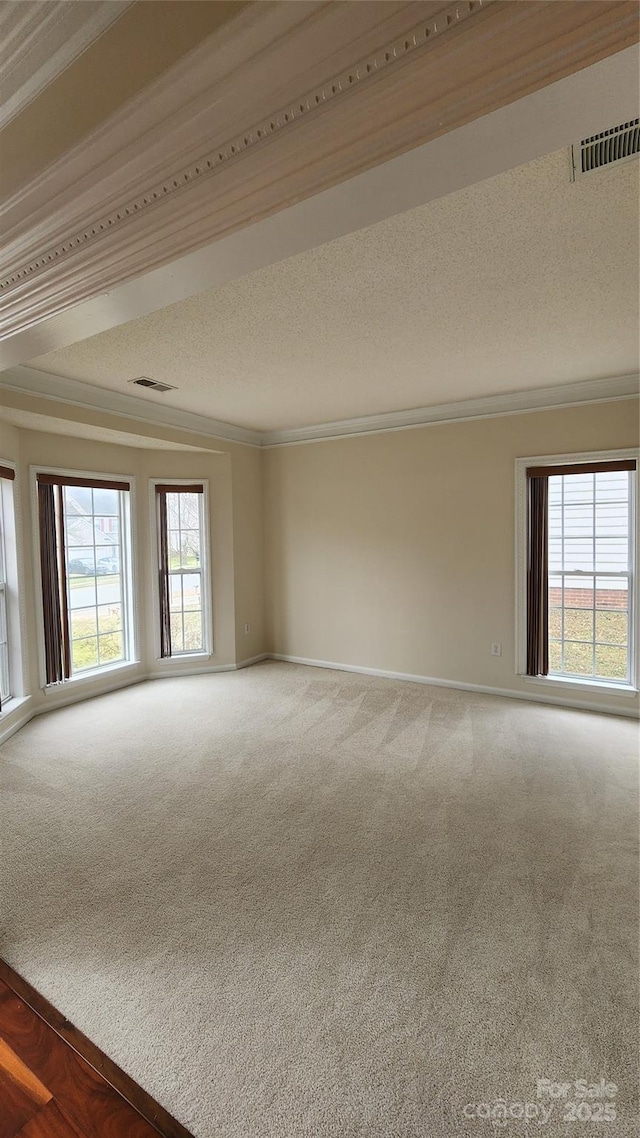 carpeted empty room featuring a textured ceiling, ornamental molding, plenty of natural light, and visible vents