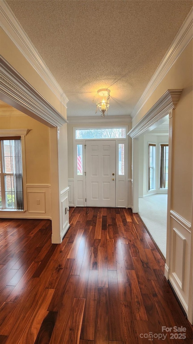 foyer entrance with dark wood-style floors, ornamental molding, and a textured ceiling