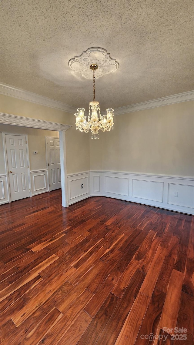 unfurnished dining area featuring a chandelier, ornamental molding, a textured ceiling, and dark wood-style floors