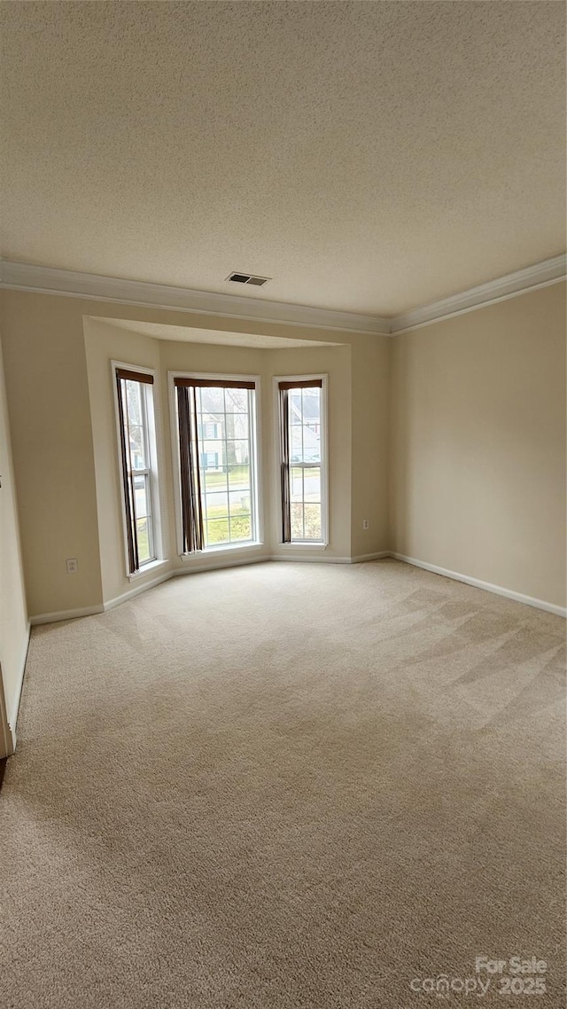 carpeted spare room with baseboards, visible vents, a textured ceiling, and ornamental molding
