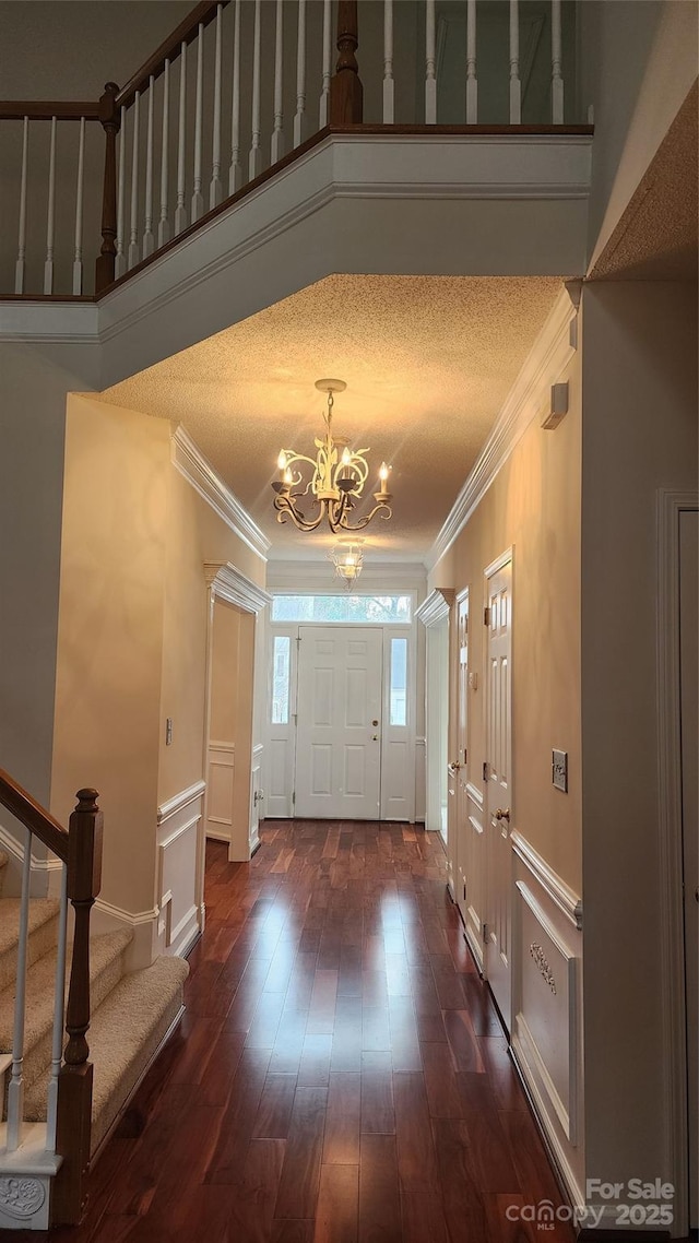 foyer entrance featuring crown molding, stairway, a decorative wall, and an inviting chandelier