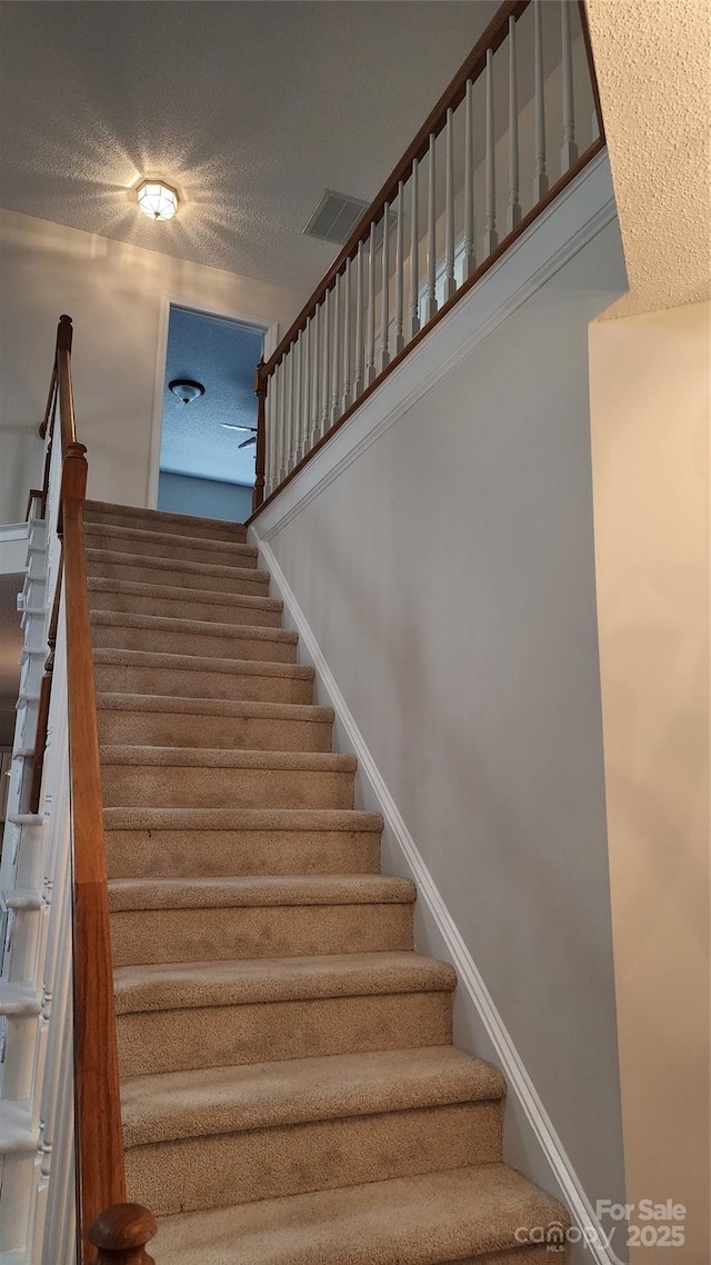 stairway with baseboards, visible vents, and a textured ceiling