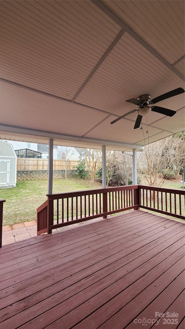deck with an outbuilding, fence, a ceiling fan, a lawn, and a storage unit