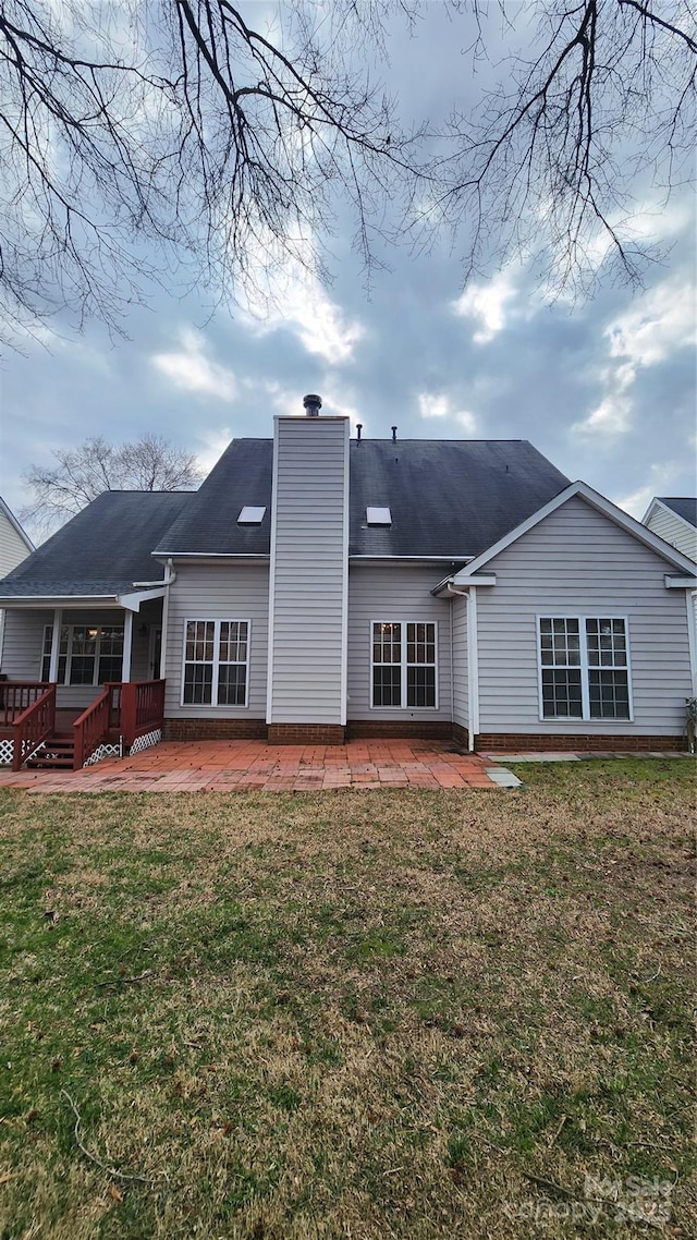 rear view of property with a deck, a yard, a chimney, and a patio area