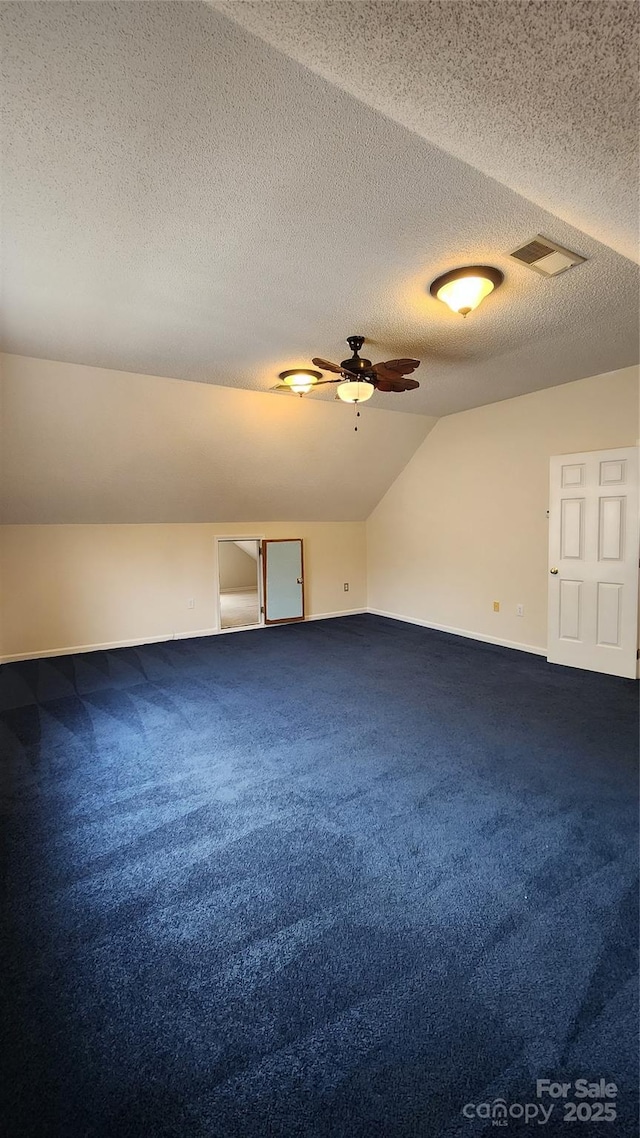 additional living space with lofted ceiling, visible vents, dark carpet, a ceiling fan, and baseboards
