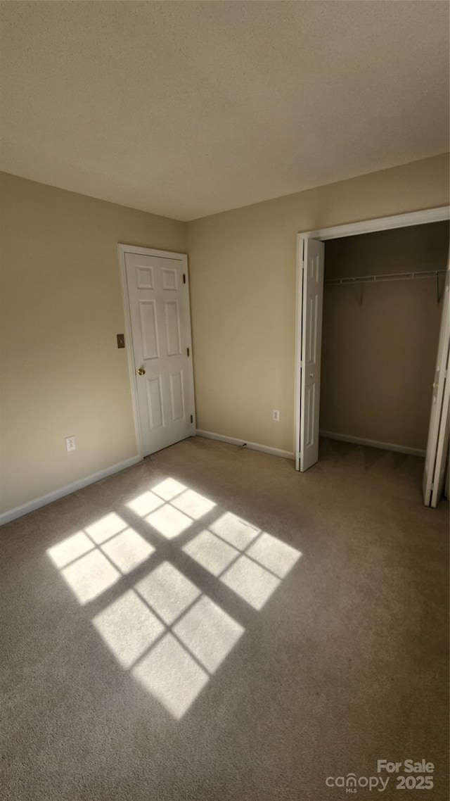 unfurnished bedroom with carpet floors, a textured ceiling, baseboards, and a closet