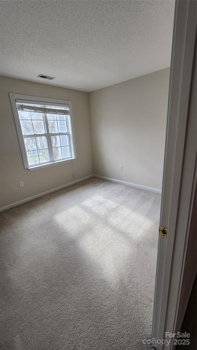 empty room featuring a textured ceiling, carpet flooring, visible vents, and baseboards