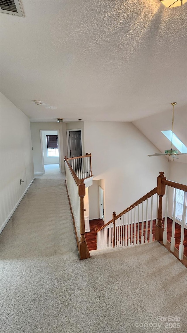 hall with carpet floors, vaulted ceiling with skylight, visible vents, and an upstairs landing