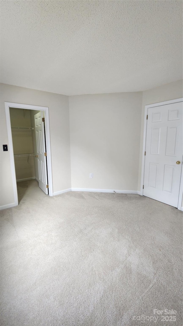 unfurnished bedroom featuring a textured ceiling, light carpet, baseboards, a closet, and a walk in closet