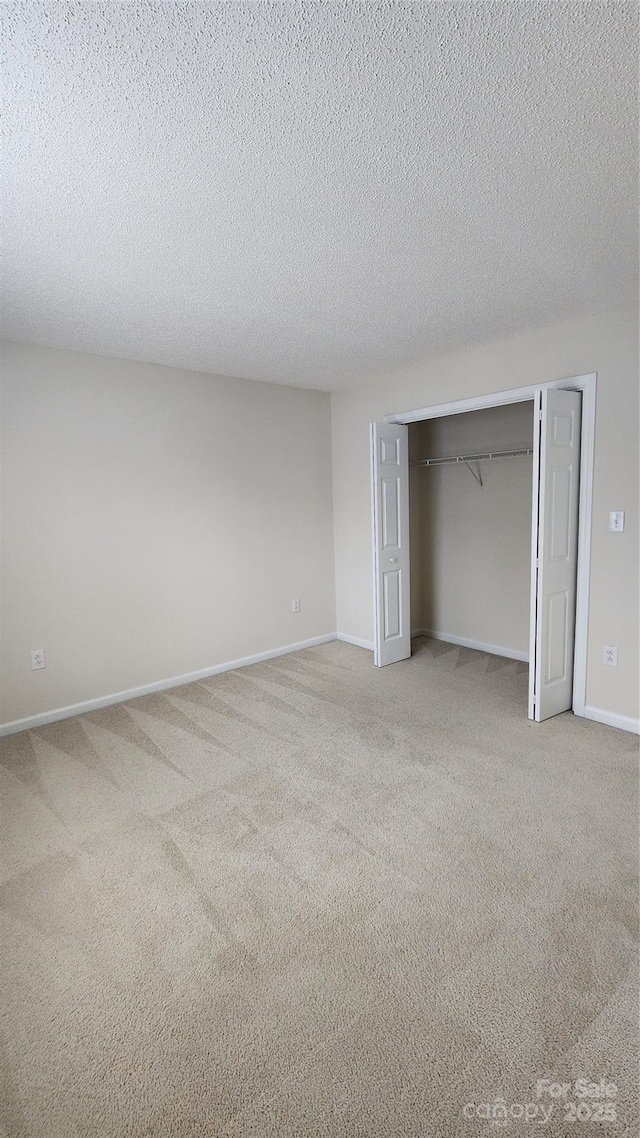 unfurnished bedroom with a closet, light carpet, a textured ceiling, and baseboards