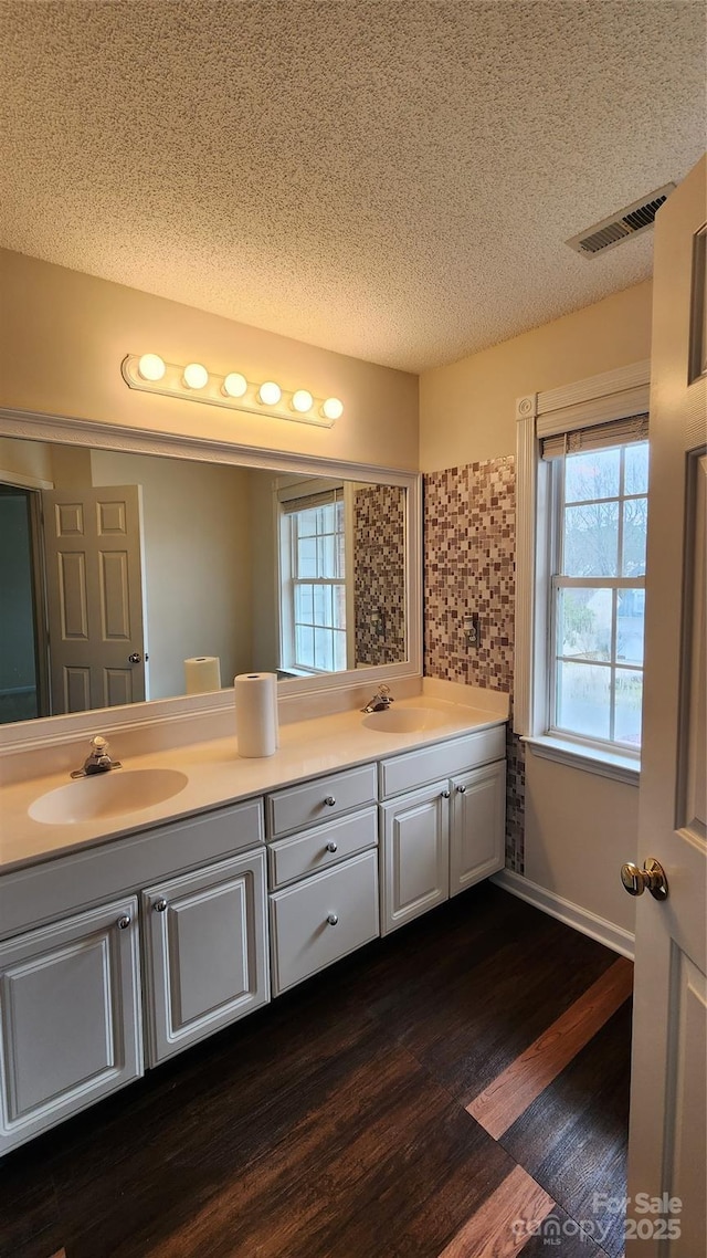 full bathroom with wood finished floors, visible vents, a sink, and double vanity
