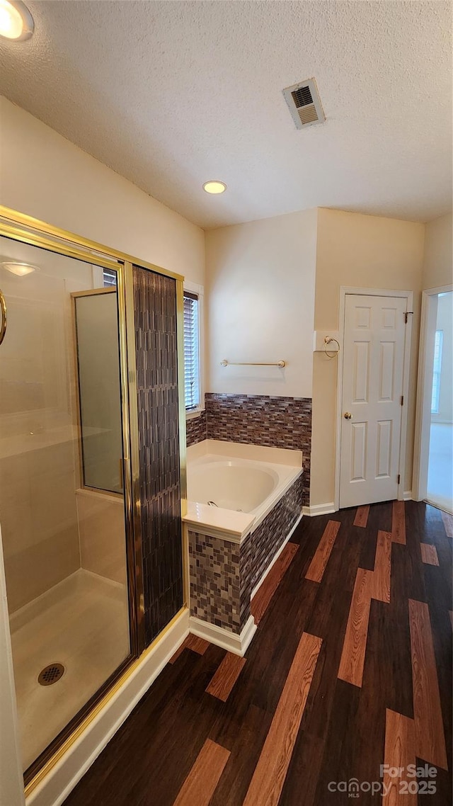 full bath with a garden tub, a textured ceiling, visible vents, and wood finished floors