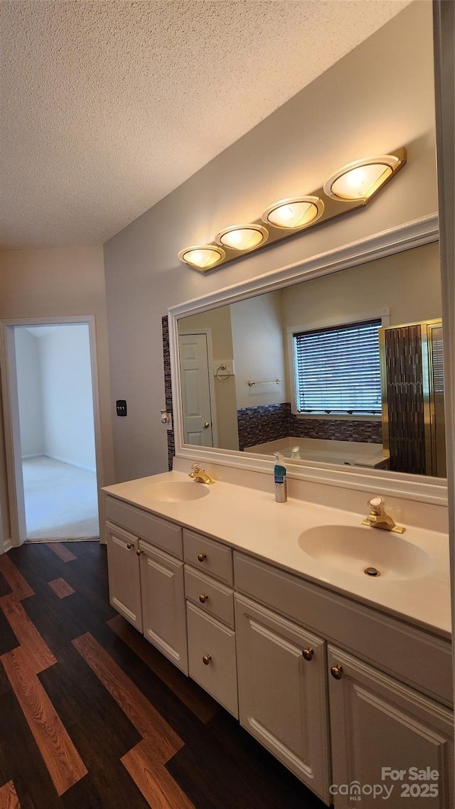 full bathroom with double vanity, a textured ceiling, a sink, and wood finished floors