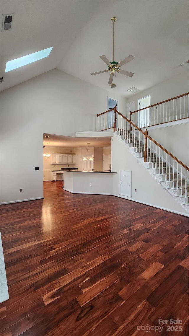 unfurnished living room featuring a skylight, visible vents, wood finished floors, high vaulted ceiling, and stairs