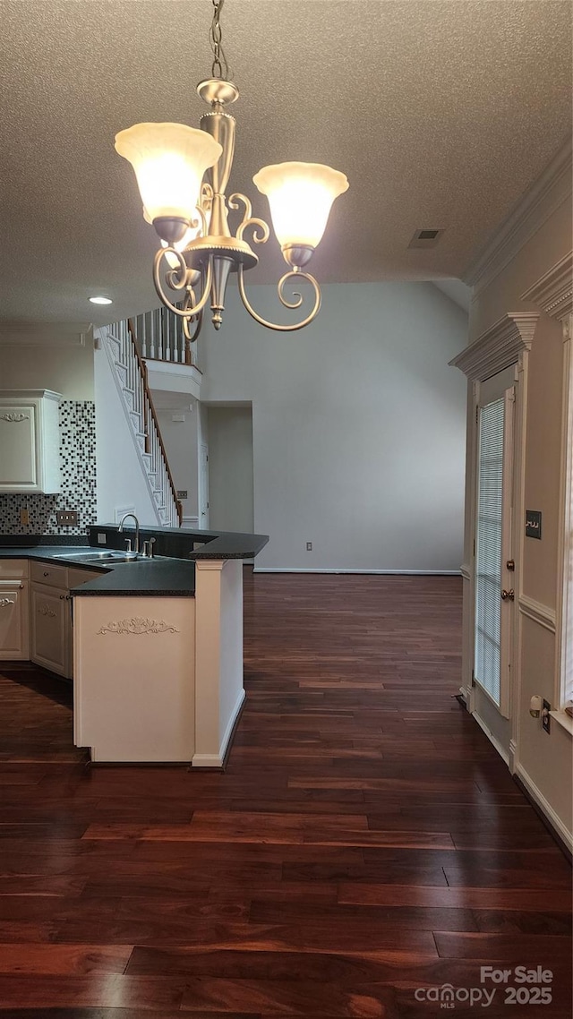 kitchen featuring a notable chandelier, tasteful backsplash, dark countertops, visible vents, and dark wood-type flooring