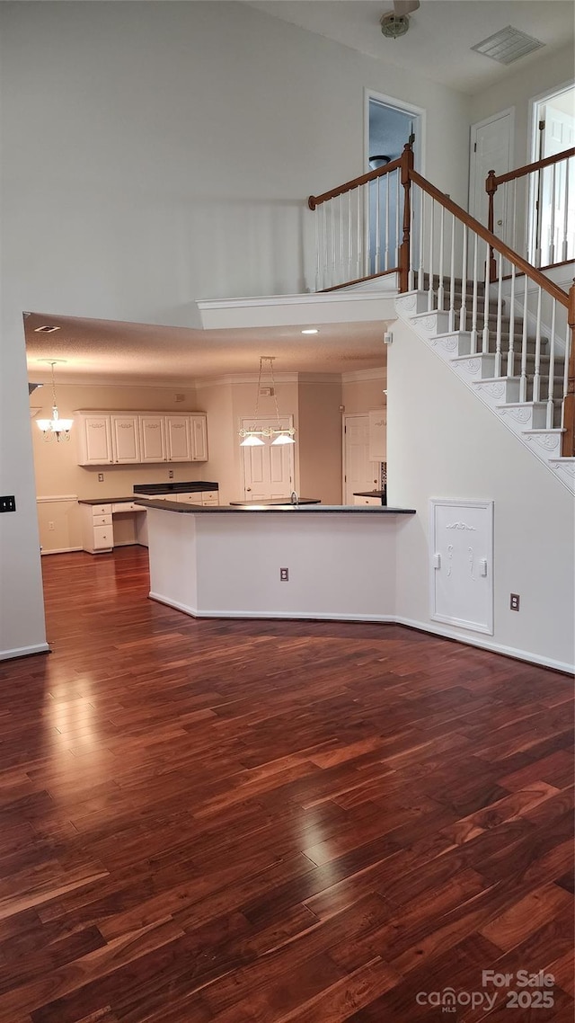 unfurnished living room with dark wood-style flooring, visible vents, stairway, and a towering ceiling