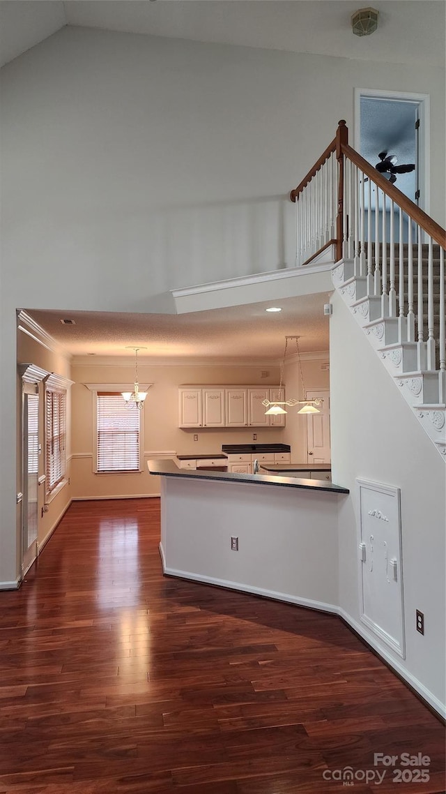 kitchen with dark wood finished floors, dark countertops, a high ceiling, pendant lighting, and a notable chandelier