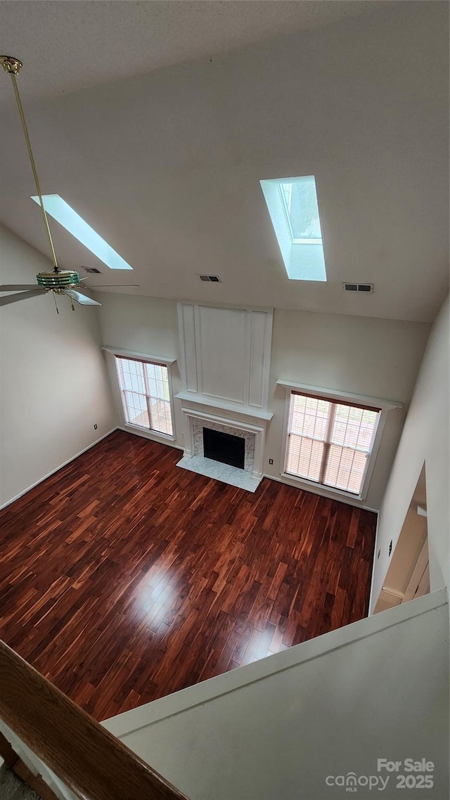 unfurnished living room with dark wood-type flooring, visible vents, a fireplace, and lofted ceiling with skylight