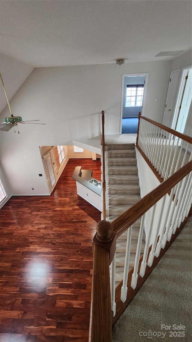 stairway featuring vaulted ceiling, a textured ceiling, and wood finished floors