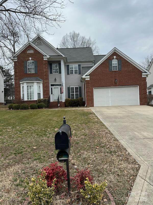 view of front of property with a garage, brick siding, driveway, and a front lawn