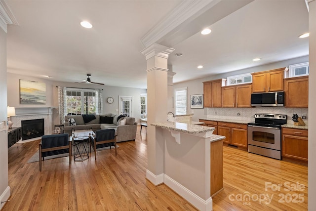 kitchen featuring light wood-type flooring, ornate columns, appliances with stainless steel finishes, and brown cabinets