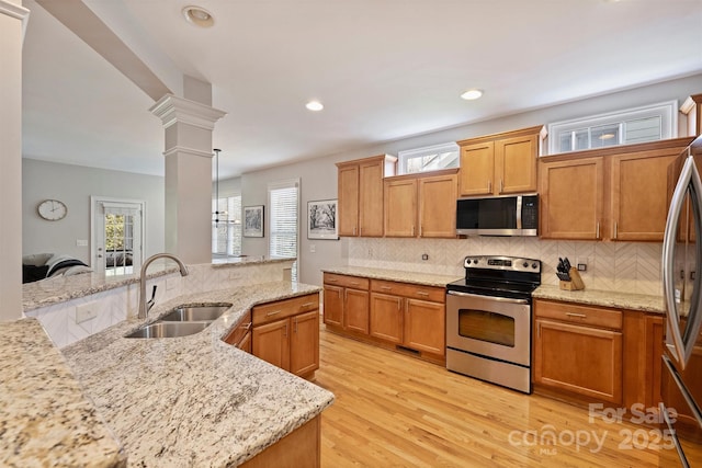 kitchen featuring tasteful backsplash, decorative columns, light wood-style flooring, stainless steel appliances, and a sink
